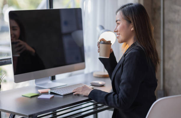 istock Smiling Asian woman drinking coffee while working online from home 1410751869