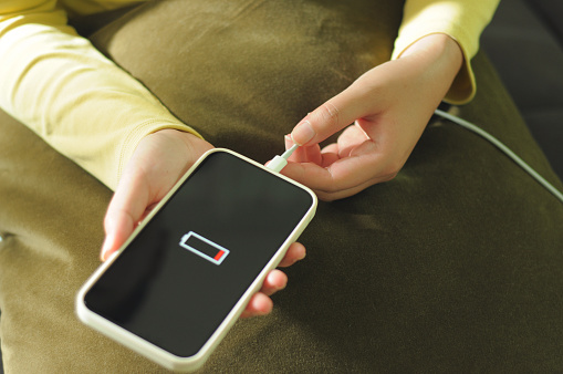 Young woman charging mobile phone battery.