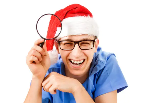 Cheerful Young Man in Santa Hat with a Magnifying Glass on the White Background