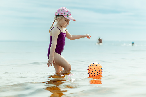 cute little girl playing with rubber ball on sand beach of Ladoga Lake. Summer beach vacation concept.