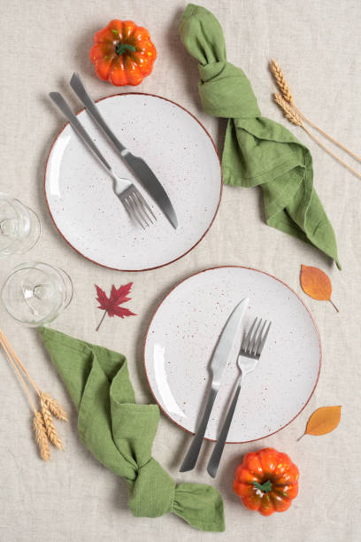 istock Thanksgiving autumn table setting for two persons. Crockery, cutlery and decorative pumpkin on beige linen tablecloth. Top view, flat lay. Selective focus. 1410753860