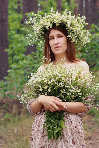 Girl with daisies. A girl in a forest in a summer dress with a bouquet of daisies and a wreath on her head. Unity with nature and its beauty