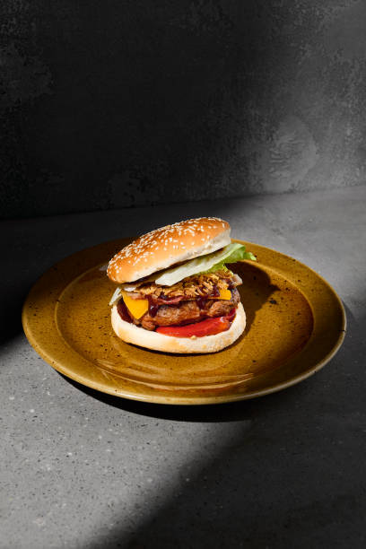 istock American burger with cheese and crispy onion on plate on gray concrete table. Beef burger with hard shadow and dark stone background. Homemade burger in dark style. Simple fast food menu. Junk food. 1410755953
