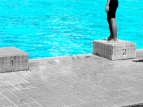 Starting block in Swimming (sport) is a raised platform mounted at the end of a pool from which swimmers begin a race. It is presented with color splash effect, black and white background. color focus on the water in the pool