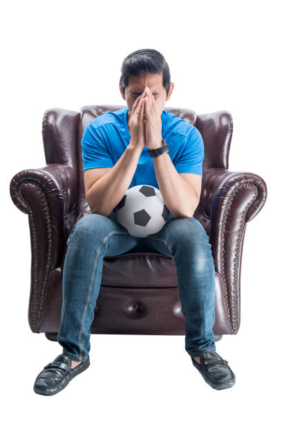 istock Asian man with the ball sitting on the couch with a disappointed expression 1410757456