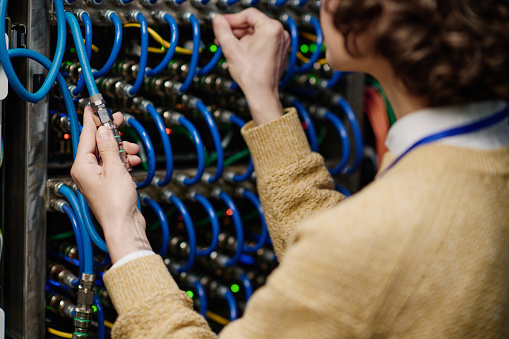 Close-up of young female engineer connecting wires in server cabinet while working with supercomputer in data center