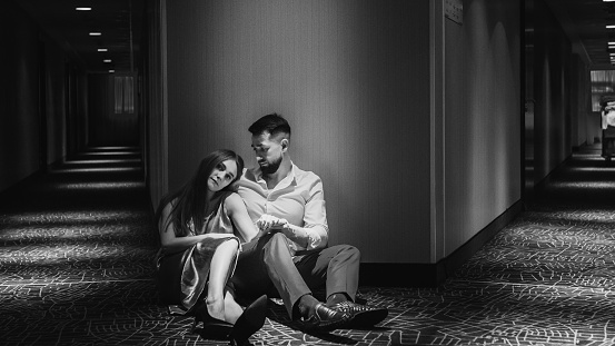 Young couple in love sitting in floor of corridor of the hotel. Black and white