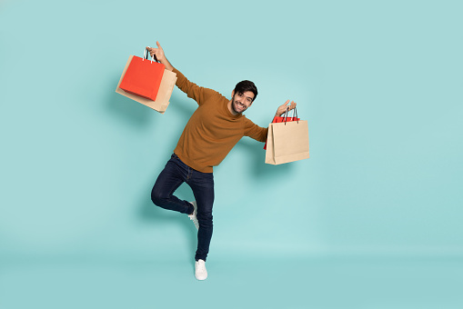 Portrait of man holding shopping bags isolated on green background, Shopper or shopaholic concept, Full length composition
