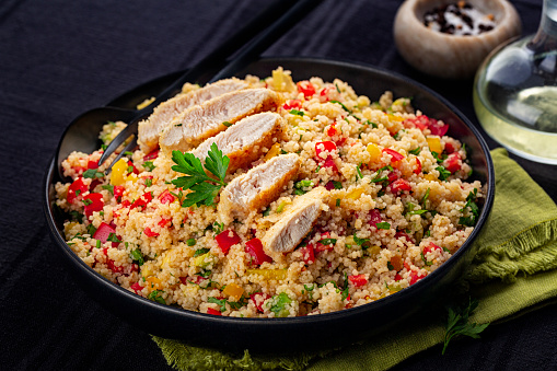 Couscous salad with Chicken breast and vegetables, tomatoes, avocado, bell pepper, parsley and lemon juice. Black table surface. Close-up.