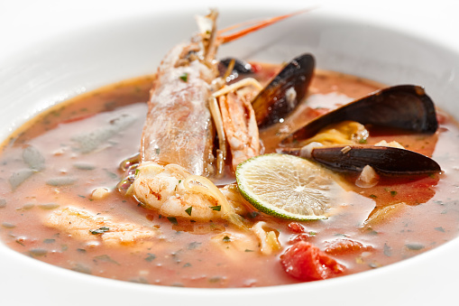 Tomato seafood soup in plate isolated on white background. Seafood stew Cioppino - shrimp,  mussels and salmon in tomato broth. Seafood dish in Italian restaurant menu