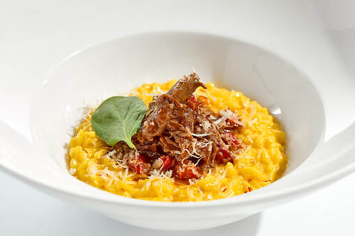 Risotto alla milanese with meat ragu. Saffron risotto with lamb meat isolated on white background. Yellow risotto in white plate. Italian classic cuisine in restaurant menu.