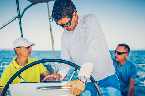 Confident skipper sailing on sailboat checking navigation route on instruments.