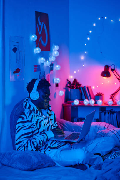 Teenager spending time for online games African teenager spending his leisure time for playing online games on laptop in his room at night neon bedroom stock pictures, royalty-free photos & images