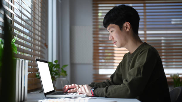 istock Side view asian male freelancer working online, browsing internet on laptop computer. 1410766193