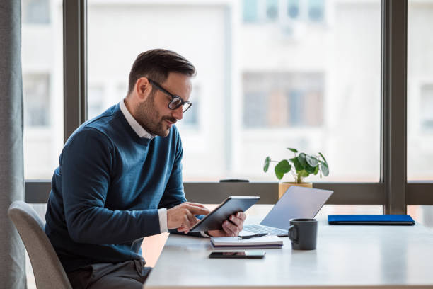 istock Businessman using digital tablet while working on laptop at office desk. 1410766356