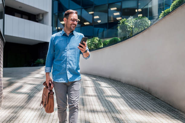 istock Happy professional messaging on cellphone while walking against office building. 1410766393