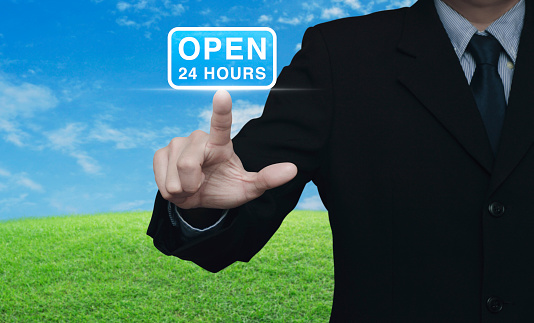 Businessman pressing open 24 hours flat icon over green grass field with blue sky, Business full time service concept