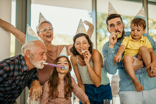 Multi generation family on birthday party in the house. Wearing birthday hats, holding sparklers, and having fun together, with a birthday cake in front of them.