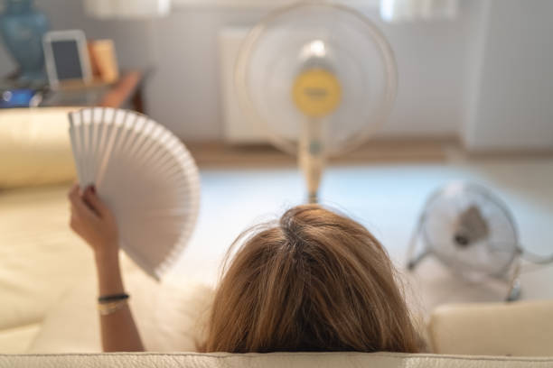 ソファに座り、数台の扇風機を手に空気と扇風機を手に、夏の気温が高い。 - summer cool electric fan heat ストックフォトと画像