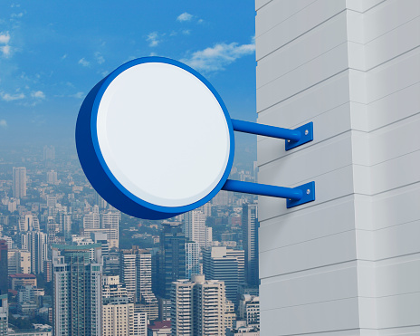 Hanging blue rounded signboard mockup over modern city tower, office building and skyscraper, Light box signage, 3D rendering