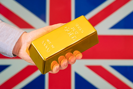The gold reserve of the Great Britain concept. Gold bar in hand on Britain flag background