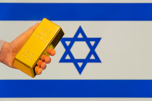 golden bullion in a man's hand on the israeli flag background