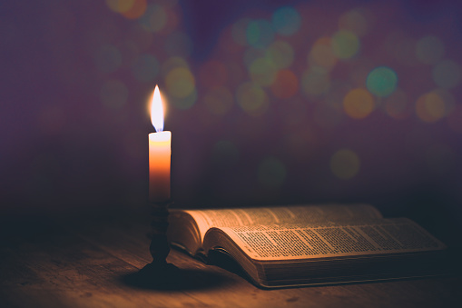 Candle with bible on a old oak wooden table. Beautiful gold background. Religion concept.