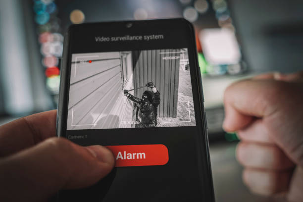 vue cctv d’un cambrioleur entrant par effraction dans la maison par une fenêtre avec pied-de-biche. protection d’un bâtiment résidentiel privé à l’aide d’un système de vidéosurveillance externe. une application sur l’écran du smartphone - cambriolage photos et images de collection