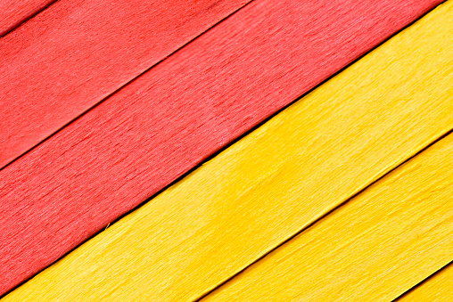 Bright yellow and red painted boards arranged diagonally. Close up wooden textured background. Textured straight planks in red and yellow.