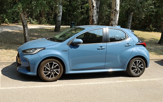 Grado, Italy. July 23, 2022. New light blue Toyota Yaris Hybrid. Side view with a public park on background.