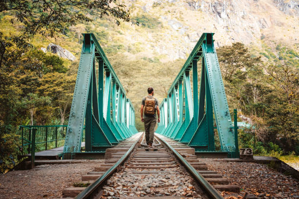 Man with backpack walking on a bridge to the town of MachuOPicchu