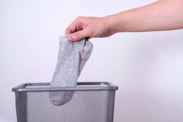 istock Man throwing an old sock with his hand into a trash can against a gray background. 1410779112