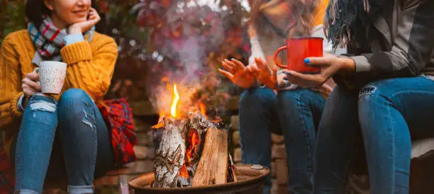 Photo of Three females best friends sitting around bonfire in casual clothes warming up and communicating