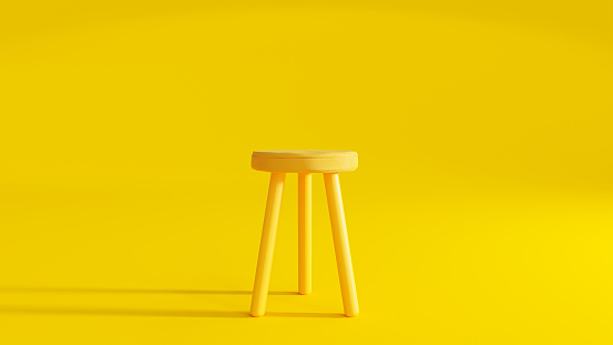 Yellow three legged chair on yellow background light from the side.