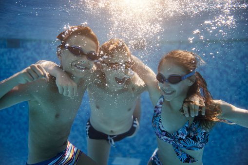 Happy teenagers having underwater party in the swimming pool. The kids are hugging and laughing. \nShot with Canon R5.