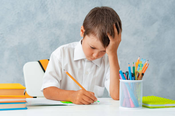 Back to school. Happy smiling student draws at the Desk. A schoolboy solves his homework. A boy from elementary school Back to school. Happy smiling student draws at the Desk. A schoolboy solves his homework. A boy from elementary school. question mark depression sitting asking stock pictures, royalty-free photos & images