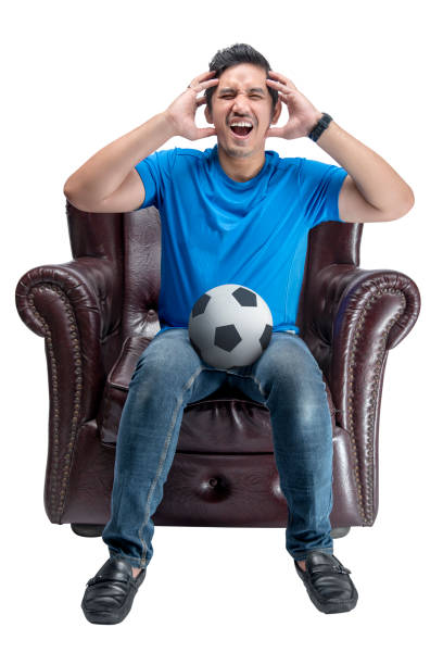 istock Asian man with the ball sitting on the couch with a disappointed expression 1410784003