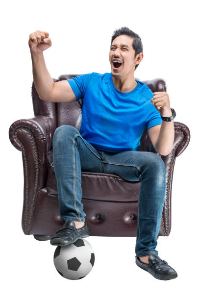 istock Asian man with the ball sitting on the couch with an excited expression 1410784099