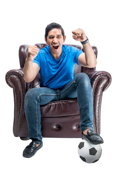 istock Asian man with the ball sitting on the couch with an excited expression 1410784120