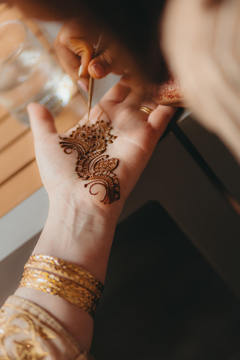 Mehendi artist painting henna art on the hand at the traditional Indian wedding ceremony.