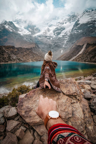 una joven pareja de vacaciones sentada en las rocas en laguna humantay, perú - provincia de cuzco fotografías e imágenes de stock