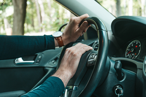 Unrecognizable young man drives his car. Human hand with watch on a steering wheel