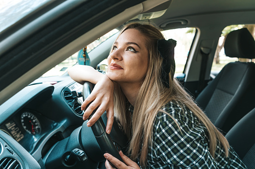 Happy young woman taking a break from driving and daydreaming in the front seat
