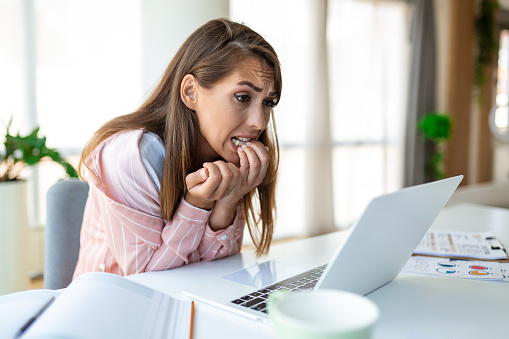 Young woman biting her nails while working on a laptop at home. Anxious woman working in office biting her fingers and nails.