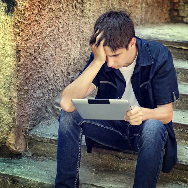 Toned Photo of Sad Teenager with Tablet Computer on the Landing Steps