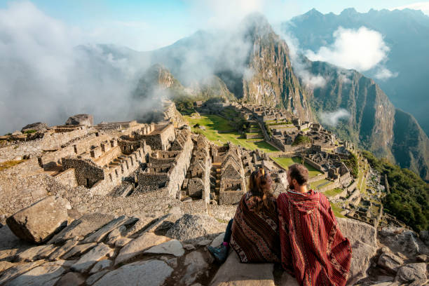couple dressed in ponchos watching the ruins of machu picchu, peru - harabe fotoğraflar stok fotoğraflar ve resimler