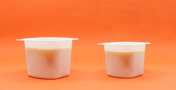 reduced yogurt on an orange background. Inflation, skimpflation or shrinkflation concept of less for the same price. reduced yogurt over an orange background. Inflation, skimpflation or shrinkflation concept of less for the same price. Shrinkflation concept, process of items shrinking in size or quantity. consumer confidence photos stock pictures, royalty-free photos & images