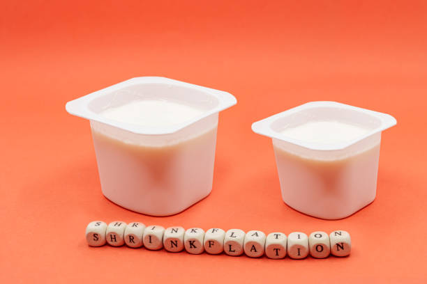 reduced yogurt on an orange background. Inflation, skimpflation or shrinkflation concept of less for the same price. Reduced yogurt over an orange background. Inflation, skimpflation or shrinkflation concept of less for the same price.reduced yogurt over an orange background. Inflation, skimpflation or shrinkflation concept of less for the same price. Shrinkflation concept, process of items shrinking in size or quantity. consumer confidence photos stock pictures, royalty-free photos & images