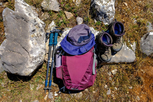 Trekking poles and hiking boots. And backpack, water bottle. Hiking gear without people. Nature, ground rock and grass. Shot from top angle.