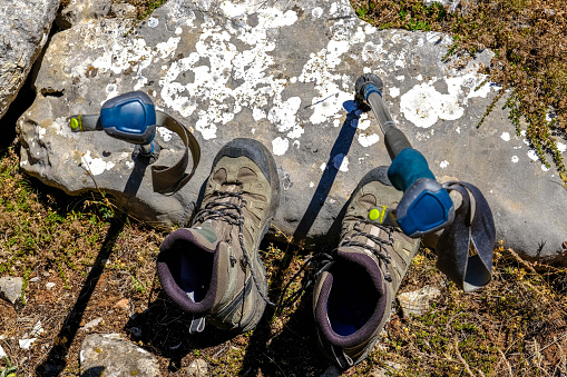 Trekking poles and hiking boots. Hiking gear without people. Nature ground rock and grass. Taken from the top angle.